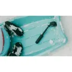 Inflation pump attached to a turquoise kayak in a snowy scene, with gloved feet visible nearby.