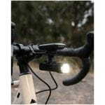 Close-up of a road bike cockpit with a Garmin bike computer and a mounted front light on the handlebars, outdoors on a trail