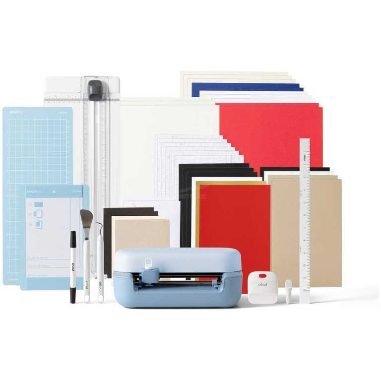 Light blue Cricut cutting machine with assorted craft mats, papers, rulers, and tools arranged behind it for scrapbooking and crafts.