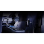 Inside a car cabin, a black wired headset is mounted on the back of the front seat while a smartphone rests on the center console nearby.