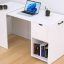 White desk with built-in storage: laptop on top, headphones on the side, and a lower cubby with books.