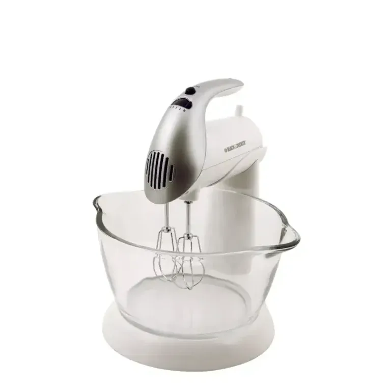 Electric handheld mixer with two beaters resting in a clear glass mixing bowl on a white surface