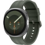 Green smartwatch with a thick olive-green strap displaying activity stats (92) and 3,457 steps, date Sat 28, on a dark screen with orange hands and markers.