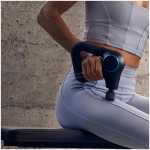 Person in light gray athletic wear using a handheld massage gun on their glute while seated on a workout bench for post-exercise recovery